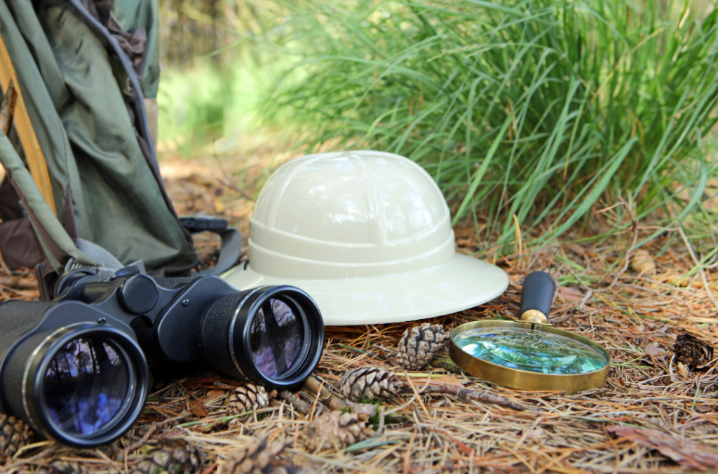binoculars, a hat, and a magnifying glass rest on the ground