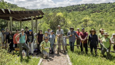 Members of the Texas Master Naturalist North Texas Chapter in a tree covered landscape with shovels and tools.